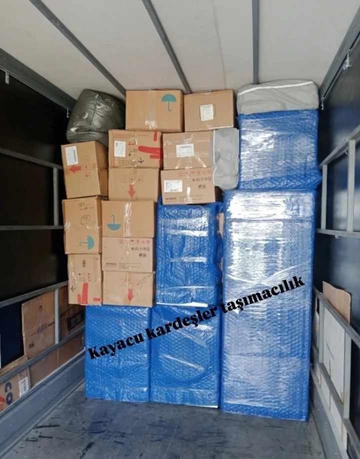Kamyonda üst üste dizilmiş koliler ve mavi paketli mobilyalar