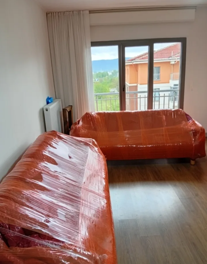 Balkon manzaralı salonda turuncu streçle korunan koltuklar