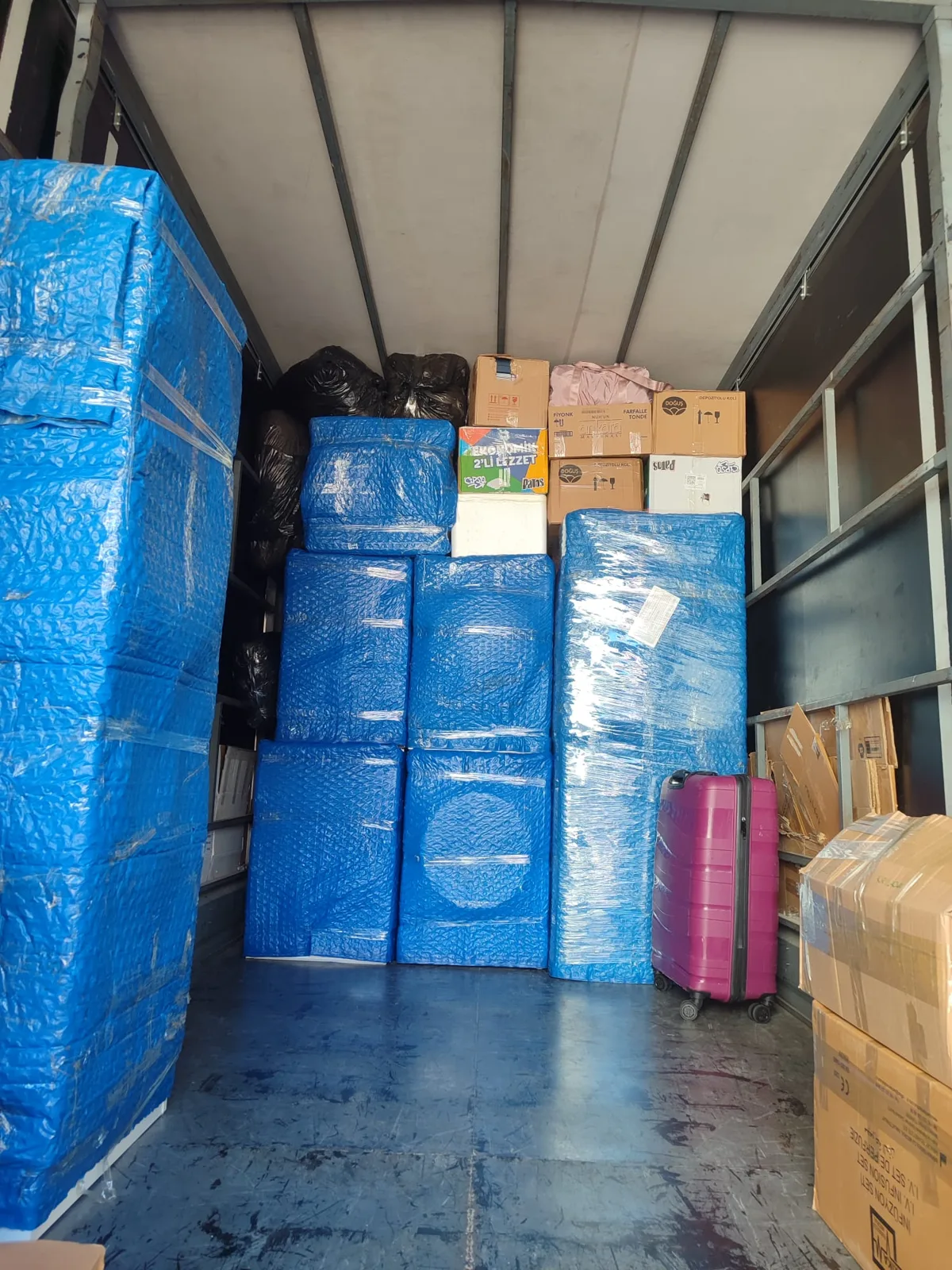 Koliler ve mavi baloncuklu naylonla paketlenmiş eşyalarla dolu nakliyat kamyonu
